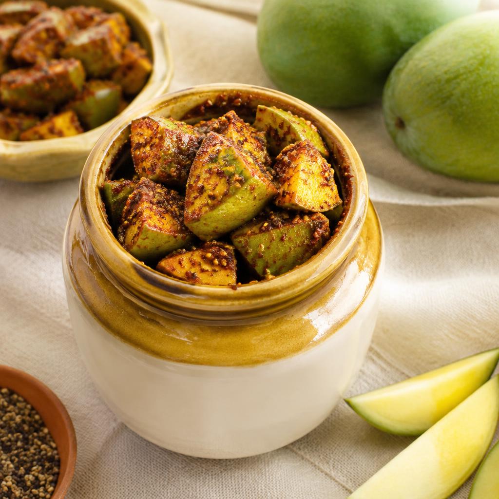 Mango pickle in a traditional ceramic jar with raw mangoes